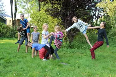 Kinder machen Akrobatik und halten sich an den Händen auf einer grünen Wiese
